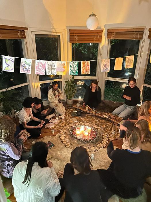 A women’s circle gathered around candles, with artwork hung above